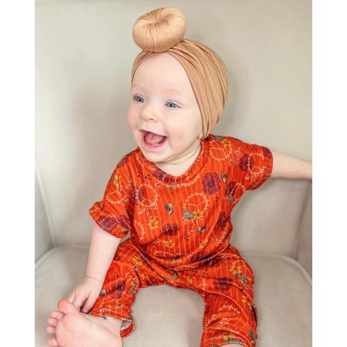A baby wearing a Tiny Knot Co - Bamboo Baby Knotted Headwrap sits on a couch.