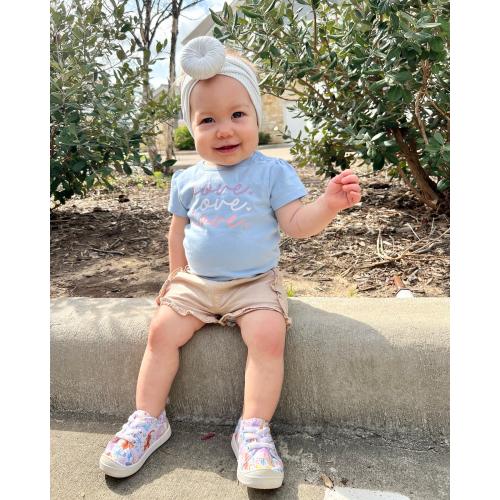 A baby girl wearing a blue t-shirt and Tiny Knot Co sneakers.