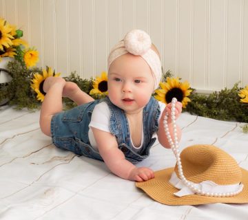 A baby laying on a blanket with a Lola, Blush - Bamboo Baby Knotted Headwrap from the Tiny Knot Co and sunflowers.