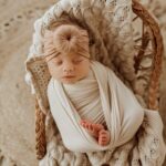 A newborn sleeping in a wicker basket with a Tiny Knot Co headband 