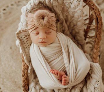 A newborn sleeping in a wicker basket with a Tiny Knot Co headband