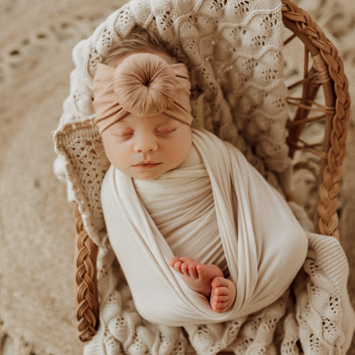A newborn sleeping in a wicker basket with a Tiny Knot Co headband