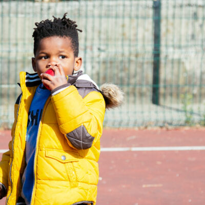A young boy in a yellow jacket holding a tennis racket for the Tiny Knot Co.