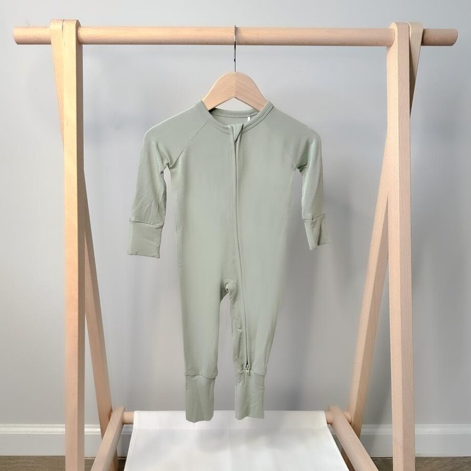 A Tiny Knot Co onesie hanging on a wooden rack.