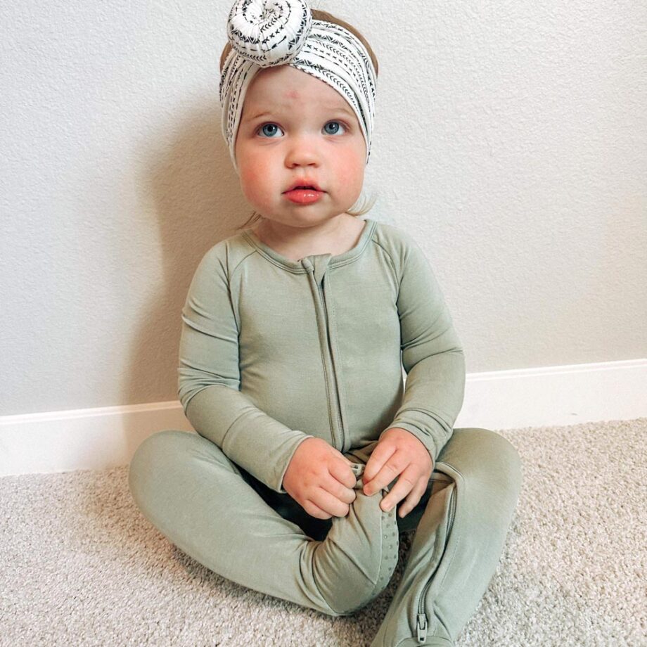 A tiny baby sitting on the floor in a green outfit with a headband from Tiny Knot Co.