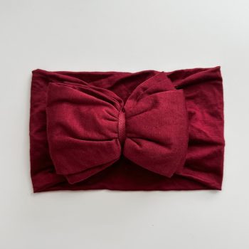 A burgundy bow headband on a white surface.
