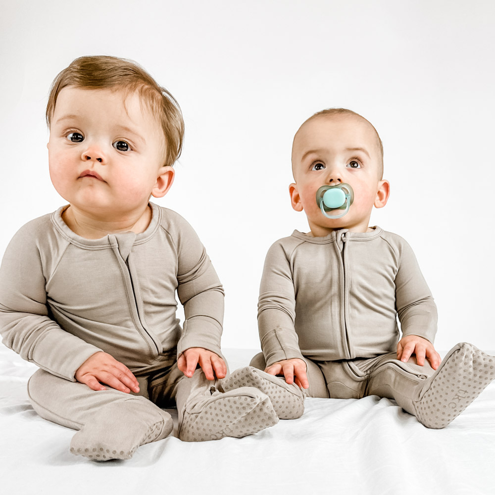 Two babies sitting on a white bed in a Homepage Rev Slider image.