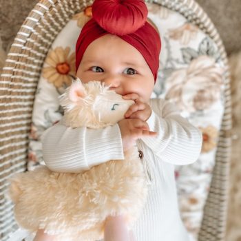 A baby wearing a Tiny Knot Co Snow - Bamboo Baby Knotted Headwrap in a wicker basket.