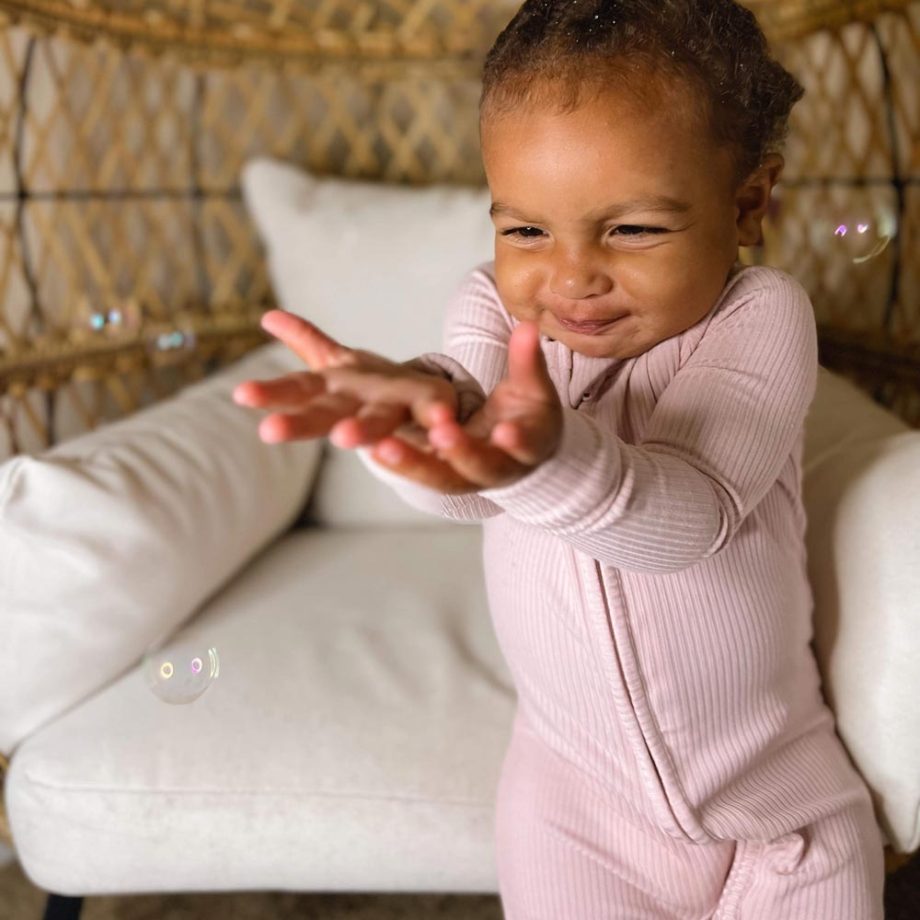 A tiny baby girl is playing with bubbles in a pink pajama.