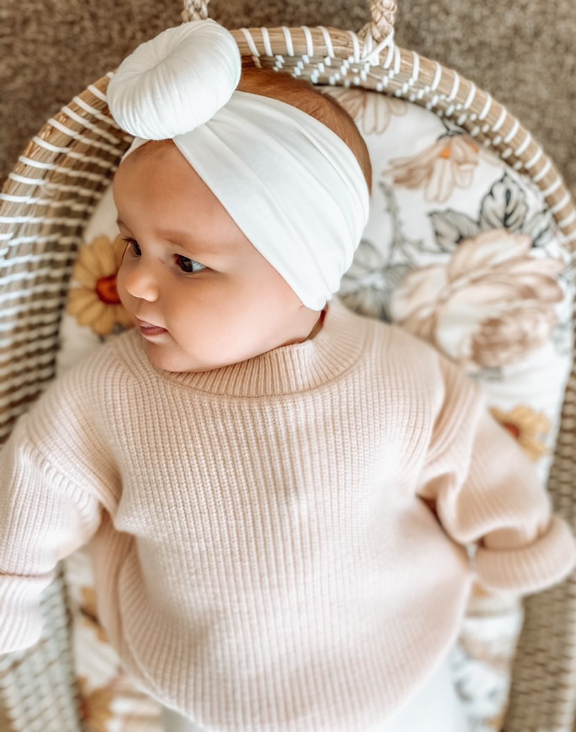A baby in a wicker basket wearing the Snow - Bamboo Baby Knotted Headwrap from Tiny Knot Co.