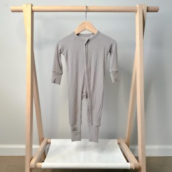 A grey baby romper hanging on a wooden rack from Tiny Knot Co.